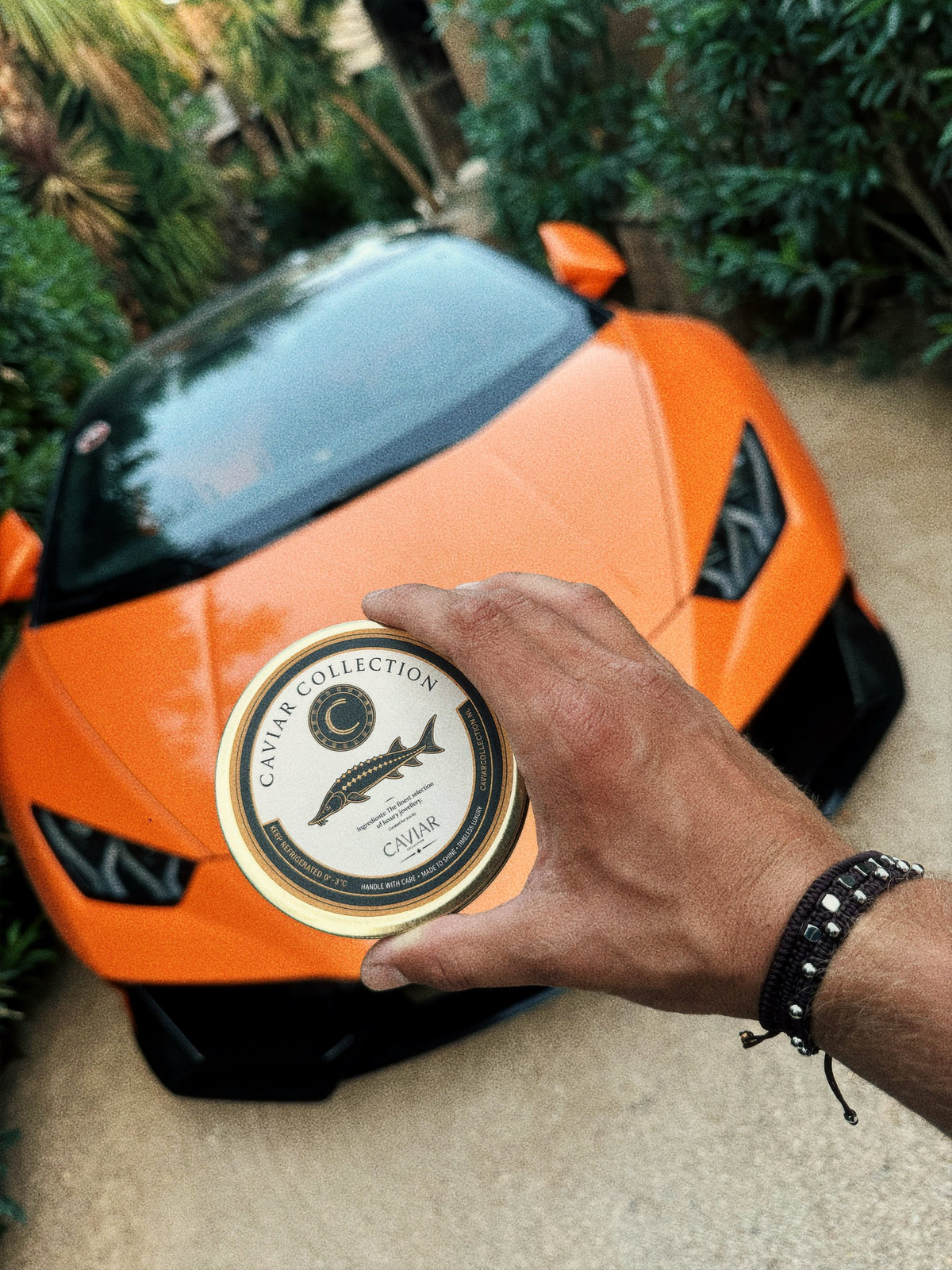 Caviar Box in de hand bij een oranje sportwagen